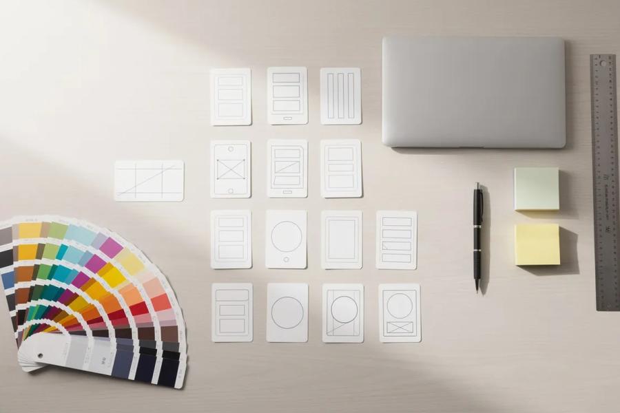 Muestras de color y tarjetas de maquetas sobre un escritorio, junto a un portátil, un bolígrafo, notas adhesivas y una regla